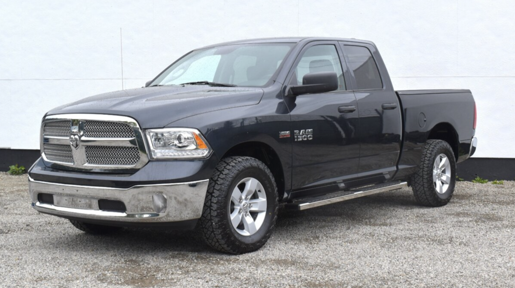 Dark gray Ram 1500 pickup truck, three-quarter front-left view with chrome grille and large tires, parked on gravel.